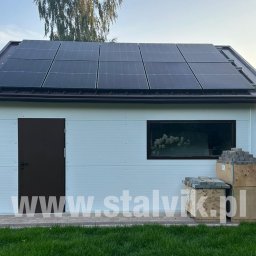 Stalvik Garaże z płyt warstwowych - Gotowa hala z paneli warstwowych z panelami solarnymi na dachu. Obok ułożone kostki brukowe. Widoczny adres strony internetowej firmy.