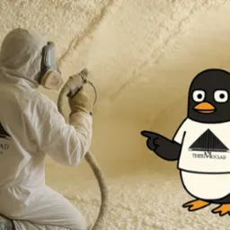 Pracownik w kombinezonie spryskuje pianą PUR ścianę, obok pingwin w koszulce z logo firmy. Nietypowe ujęcie procesu ocieplania pianką.