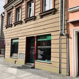 Fasada biura rachunkowego w kamienicy z zielonymi ramami okiennymi i czerwonymi elementami dekoracyjnymi. Na oknie widoczne informacje o usługach.