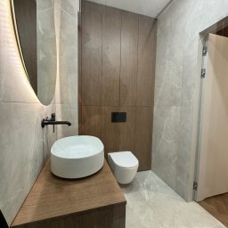 WroTeam Meble sp. z o.o. - Nowoczesna łazienka we Wrocławiu: umywalka nablatowa na szafce z drewna, podświetlane lustro, płytki imitujące marmur i zabudowa z drewnianych paneli.