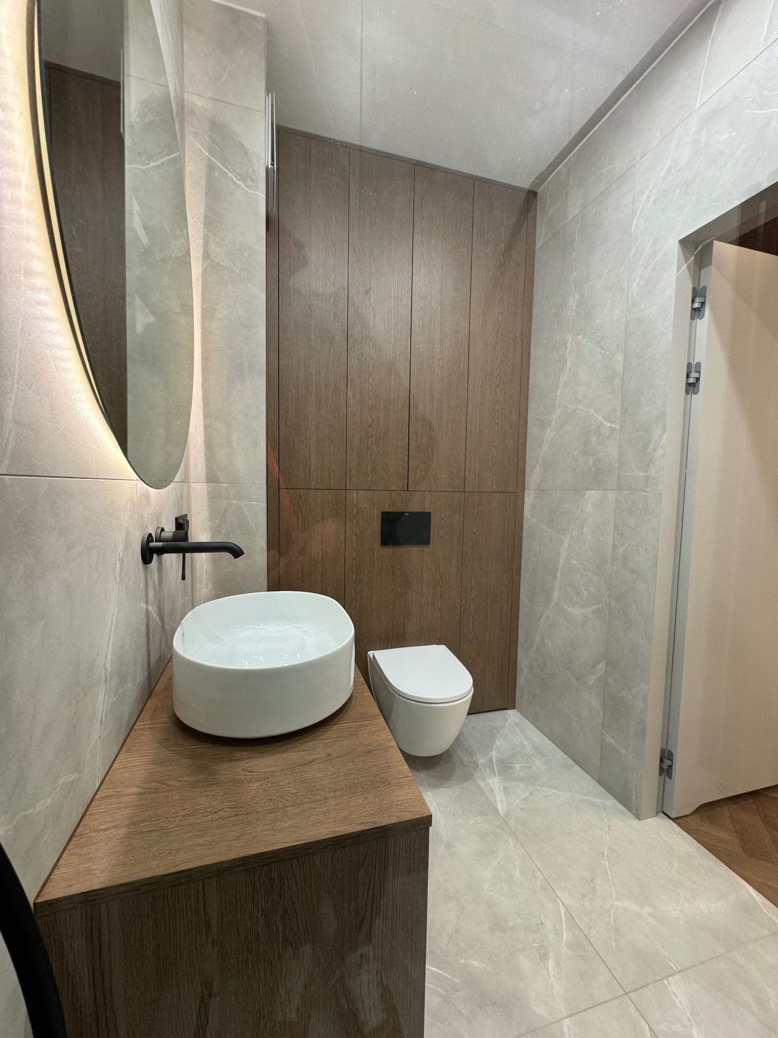 Nowoczesna łazienka we Wrocławiu: umywalka nablatowa na szafce z drewna, podświetlane lustro, płytki imitujące marmur i zabudowa z drewnianych paneli.