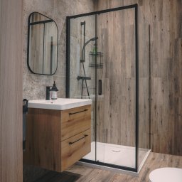 P.H.U. Konrad Kiełkowski - Nowoczesna łazienka z kabiną prysznicową w czarnej ramie, drewnianą szafką pod umywalką i lustrem. Płytki imitujące drewno na podłodze i ścianach.