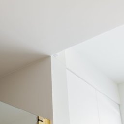 P.H.U. Konrad Kiełkowski - Minimalistyczne wnętrze: białe ściany, sufit z kwadratową, złotą lampą w rogu, podkreślające nowoczesny design.