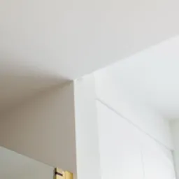 Minimalistyczne wnętrze: białe ściany, sufit z kwadratową, złotą lampą w rogu, podkreślające nowoczesny design.