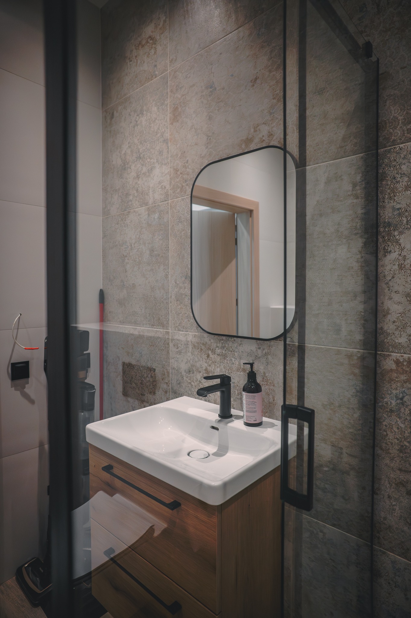 Nowoczesna łazienka z umywalką nablatową, drewnianą szafką i lustrem w czarnej ramie. Płytki imitujące kamień na ścianach, kabina prysznicowa z czarnymi profilami.