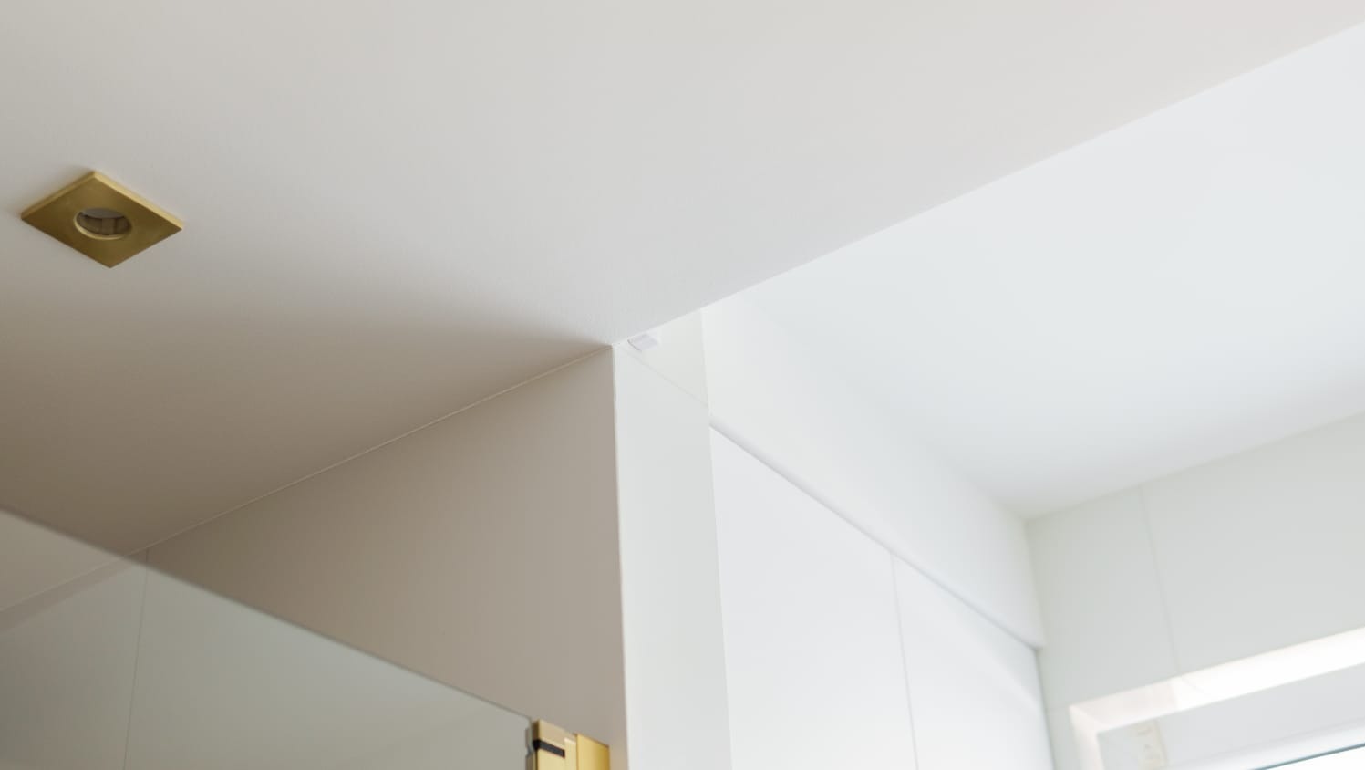 Minimalistyczne wnętrze: białe ściany, sufit z kwadratową, złotą lampą w rogu, podkreślające nowoczesny design.