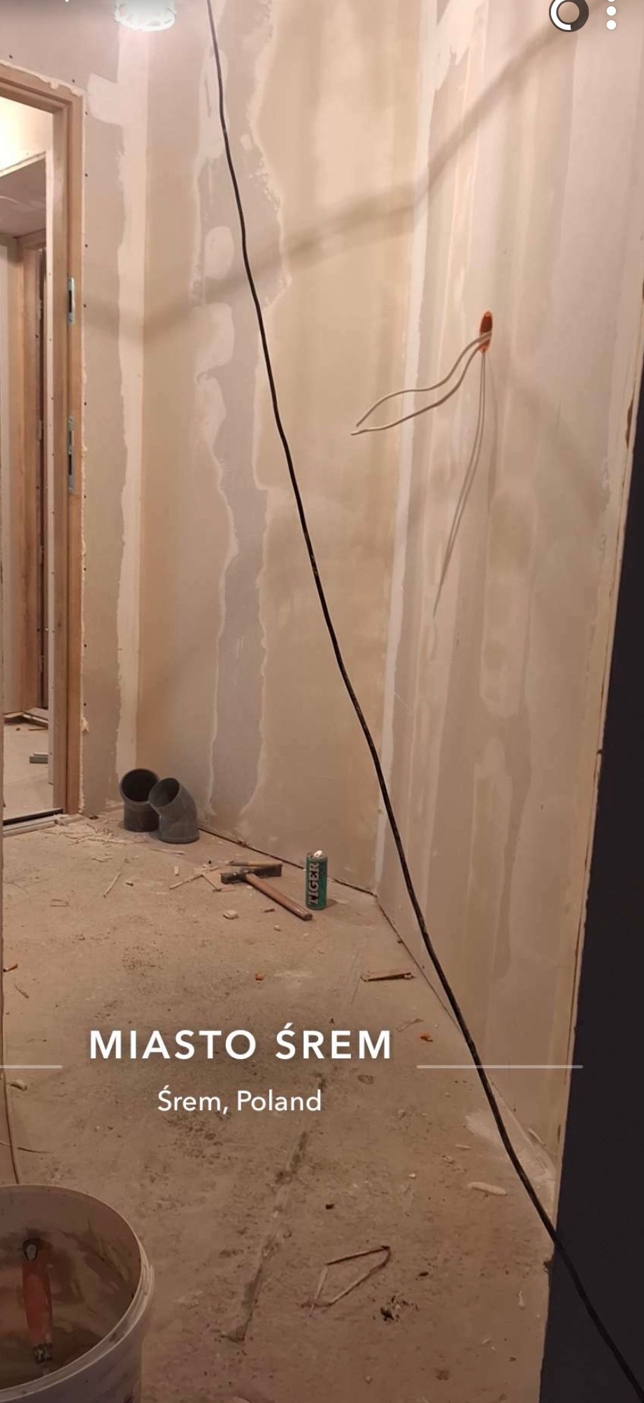 Ściany po szpachlowaniu, widoczne kable elektryczne, rury kanalizacyjne, młotek i puszka. Prace wykończeniowe w trakcie remontu mieszkania.