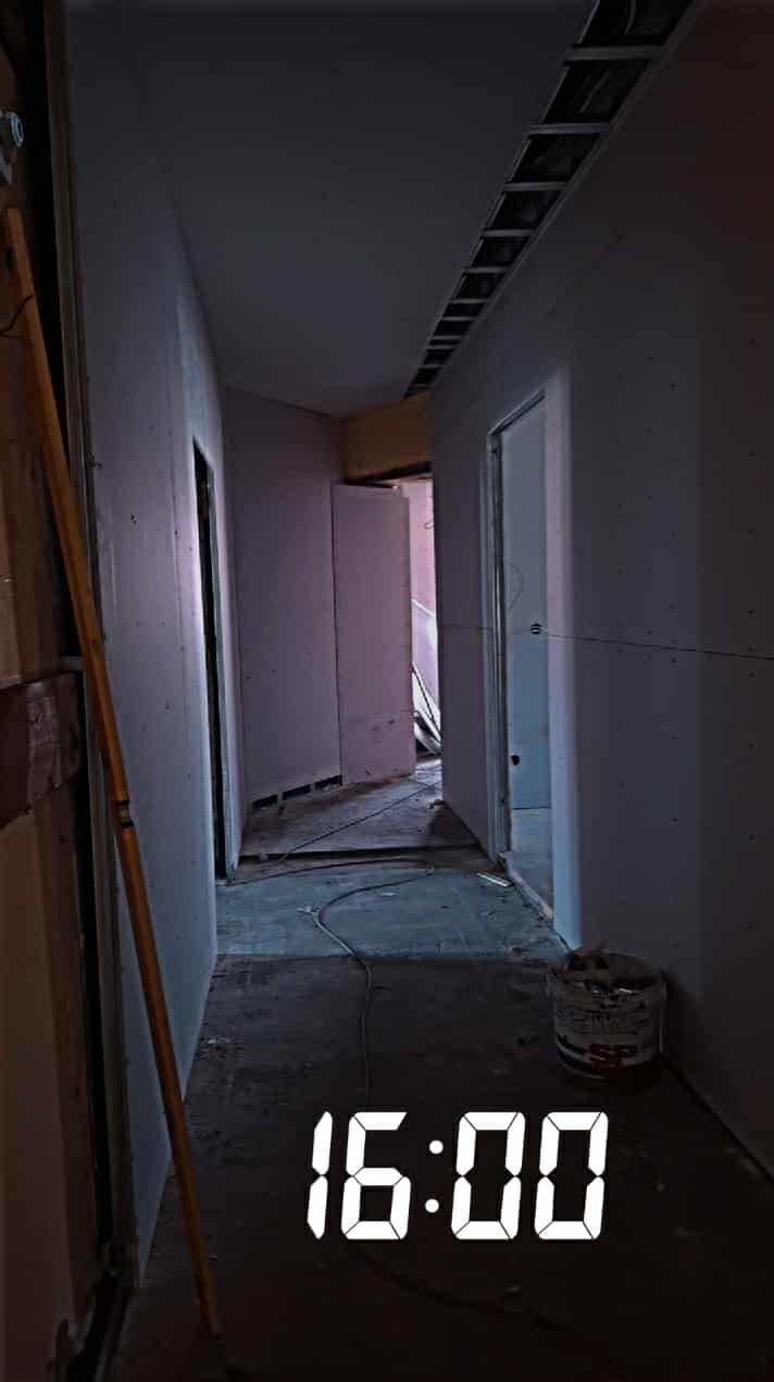 Korytarz w trakcie remontu: ściany z płyt gipsowo-kartonowych, sufit częściowo podwieszany, widoczne profile i puszka z narzędziami. Na podłodze kabel.