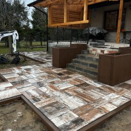 ZIBI BRUK Filip Walas - Nowa, częściowo ułożona nawierzchnia z kostki brukowej w odcieniach brązu i bieli, z obrzeżami. W tle widoczny mini-koparka i elementy architektury ogrodowej.