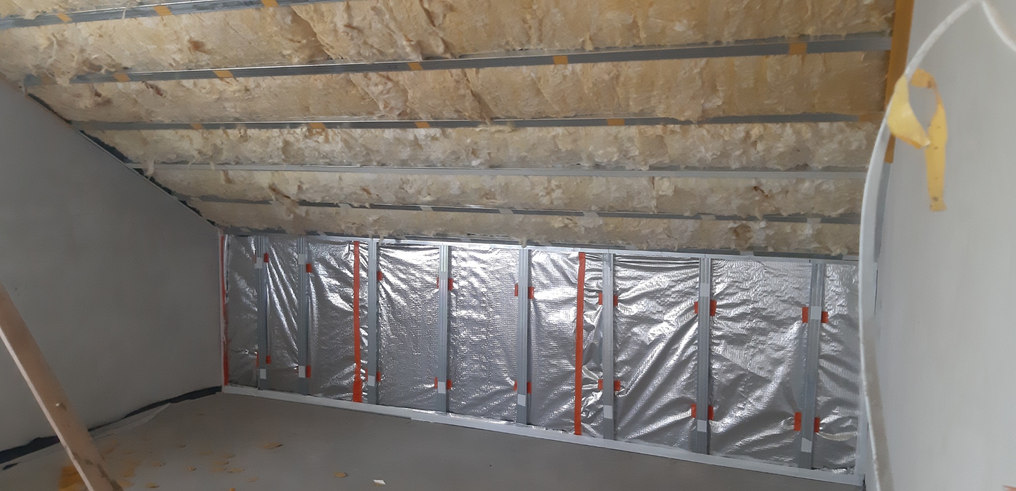 Izolacja poddasza wełną mineralną i folią aluminiową, widoczne metalowe profile. Prace wykończeniowe na poddaszu, sufit skośny.