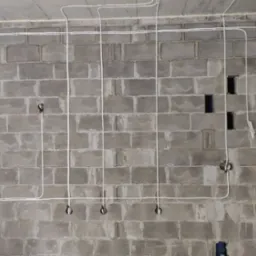 Szara ściana z betonu komórkowego z poprowadzoną białą instalacją elektryczną. Widoczne puszki instalacyjne i przewody ułożone wzdłuż ściany i pod sufitem.