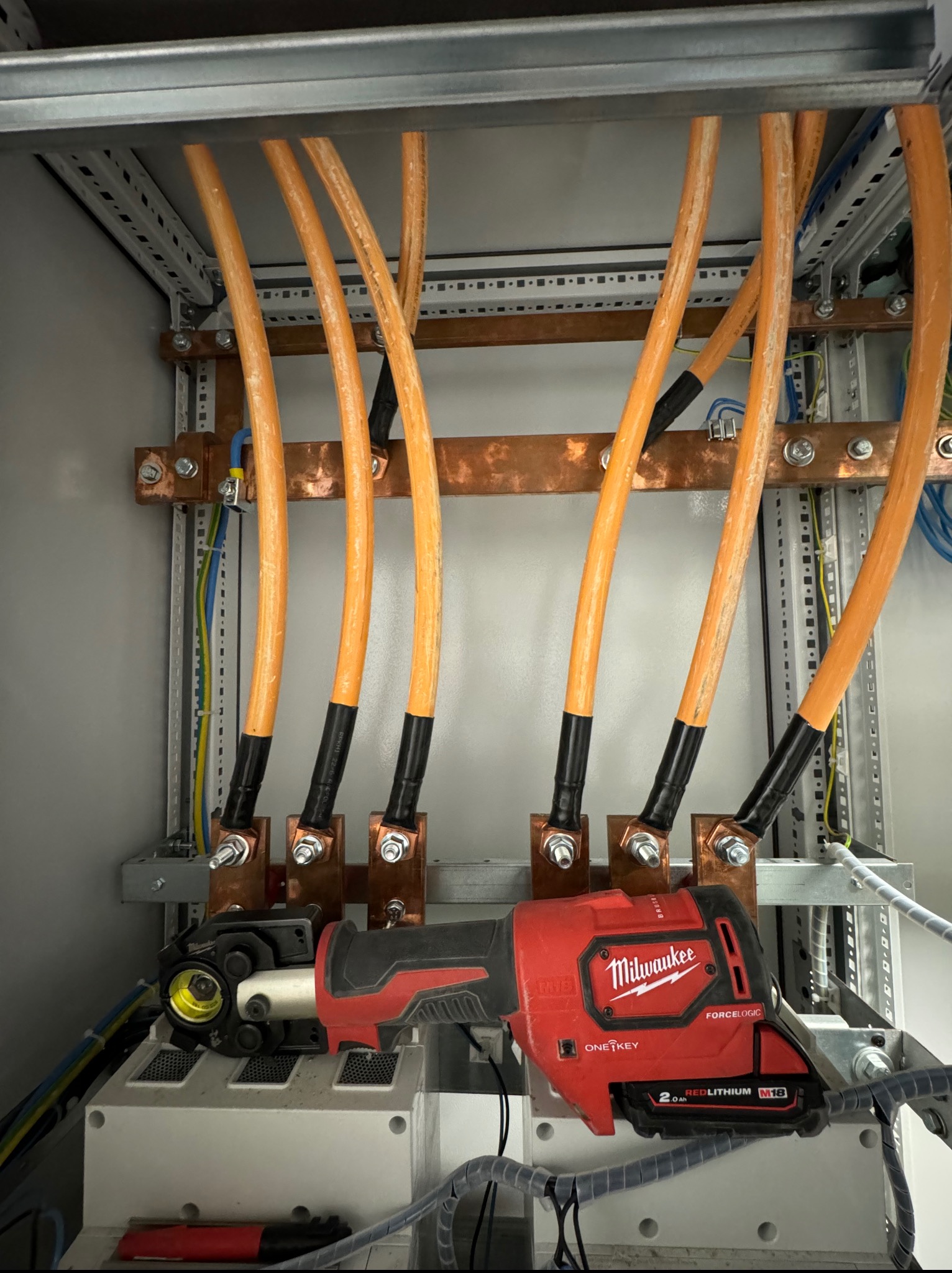 Rozdzielnia elektryczna z zamontowanymi przewodami i narzędziem Milwaukee FORCELOGIC, widok z bliska na etapie łączenia przewodów.