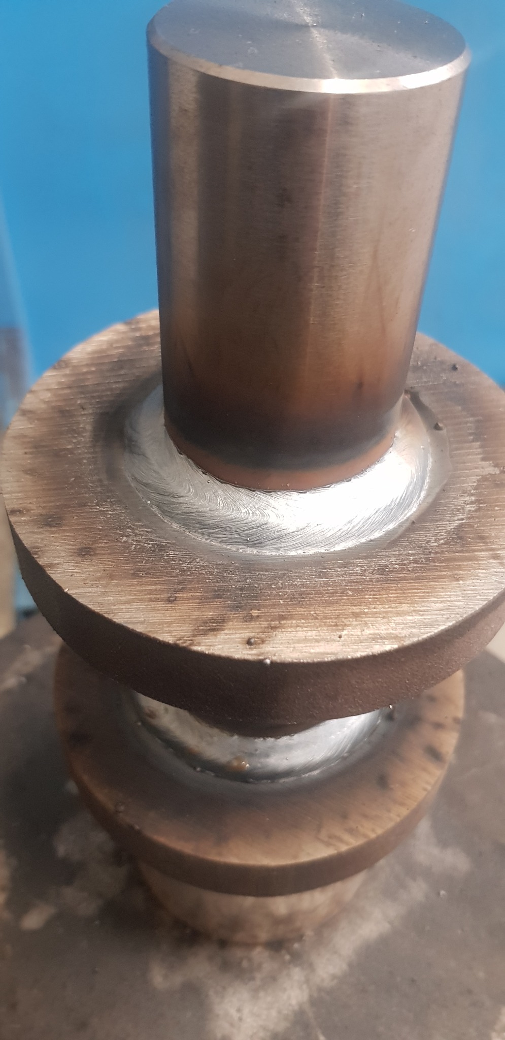 Precyzyjne spawanie dwóch metalowych elementów o okrągłym przekroju, widoczne ślady obróbki termicznej i charakterystyczny wzór spoiny. Detal z bliska.