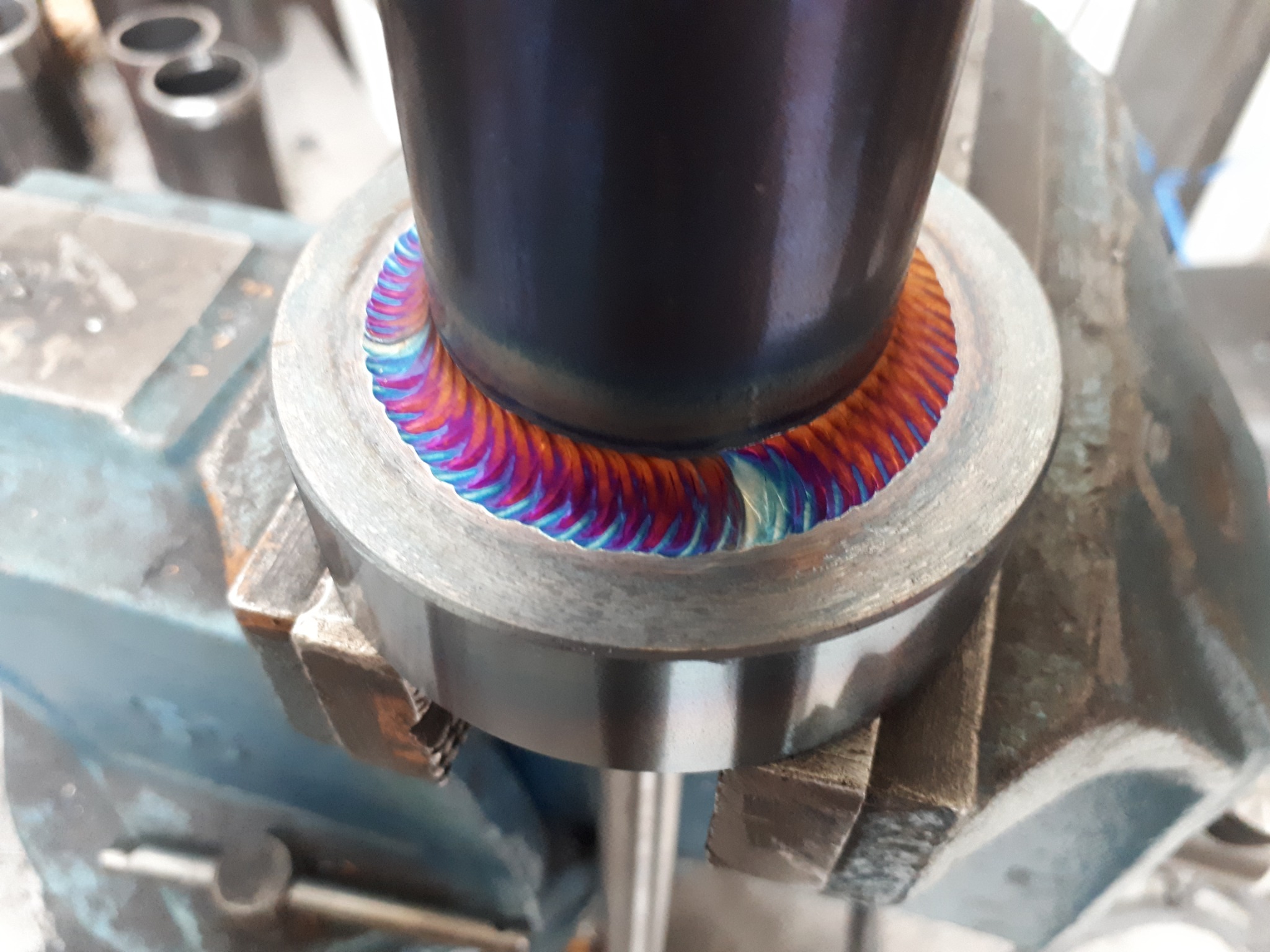 Precyzyjne spajanie metalowych elementów w uchwycie imadła, z widocznymi tęczowymi przebarwieniami spoiny, świadczącymi o wysokiej jakości wykonania.