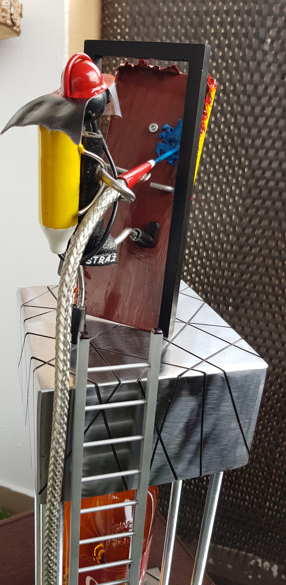 Metalowa figurka strażaka z drabiną, hełmem i wężem, stylizowana na pracę artystyczną. Nietypowy prezent dla strażaka. Dekoracja z metalu.