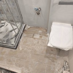 Paweł Sawicki - Remontowana łazienka z zabezpieczoną kabiną prysznicową i toaletą. Widoczne płytki imitujące drewno na podłodze i przygotowane przyłącza wodne na ścianie.