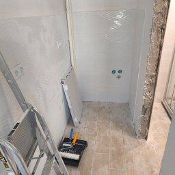 Paweł Sawicki - Biała łazienka w trakcie remontu: świeżo położone płytki z falistym wzorem, drabina malarska, narzędzia malarskie i płyta gipsowa.