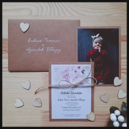 BK Graphic Life - Ręcznie robione zaproszenie na chrzest z fotografią dziecka, brązowa koperta z napisem, ozdobne serduszka na drewnianym tle. Styl rustykalny, delikatne kwiatowe motywy.