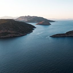Adam Żurawicki - Panoramiczny widok na morze z kilkoma małymi, skalistymi wyspami i odległym miastem na wzgórzu w tle, uchwycony o świcie.