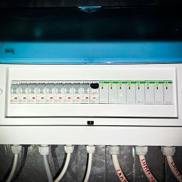 DP spółka z o.o. spółka kom. - Biała rozdzielnica elektryczna z otwartą niebieską pokrywą, ukazująca bezpieczniki EATON i moduły BIS-411 z zielonymi diodami, oraz podłączone kable opisane 'LAMPY' w Koszalinie.