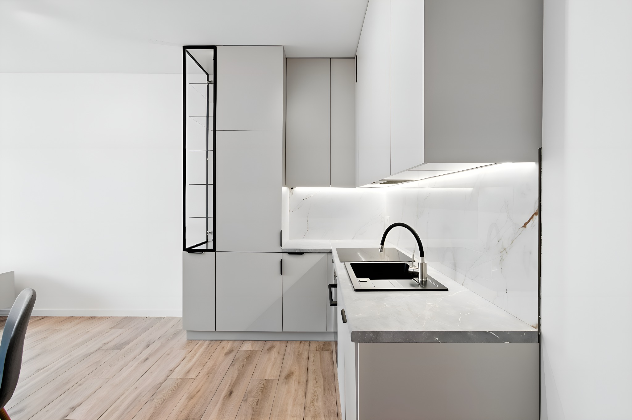 Nowoczesna kuchnia w odcieniach szarości i bieli z marmurowym blatem i drewnianą podłogą. Minimalistyczny design z czarnymi akcentami. Oświetlenie LED podkreśla elegancję.