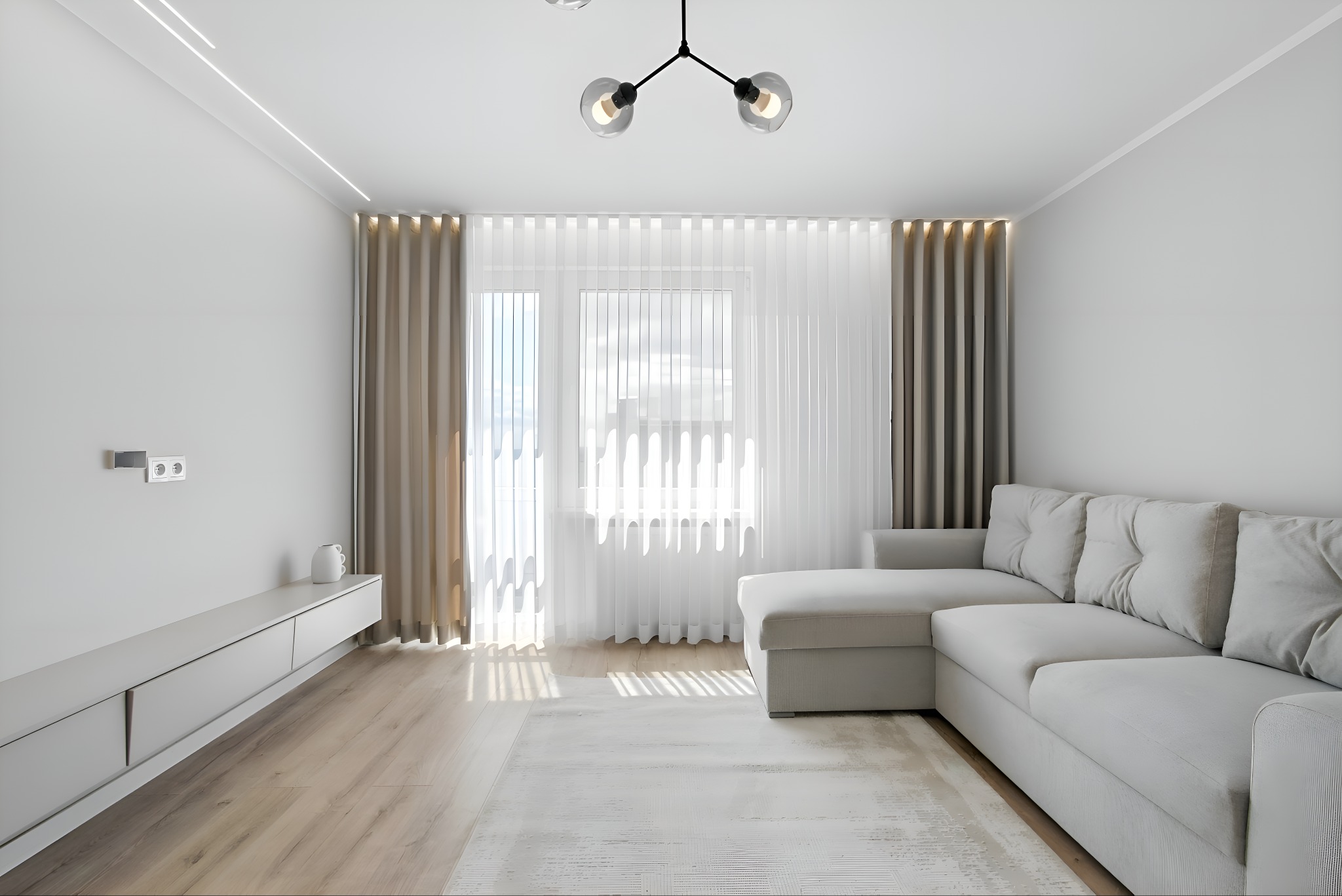 Jasny salon z szarą sofą narożną, minimalistyczną szafką RTV i zasłonami, oświetlony naturalnym światłem wpadającym przez okno.