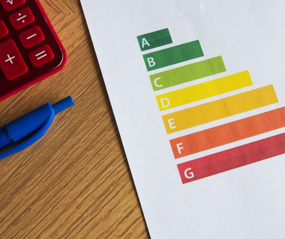 Wydruk klas energetycznych A-G z kalkulatorem i długopisem na drewnianym biurku. Dokument z kolorowymi paskami i literami symbolizującymi efektywność energetyczną.