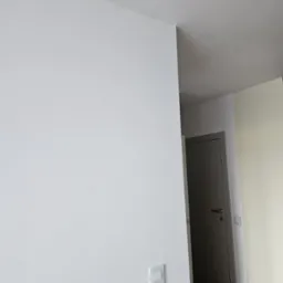 Ściana po malowaniu na biało z widocznym włącznikiem światła. W tle drzwi i fragment podłogi. Minimalistyczne wykończenie wnętrza.