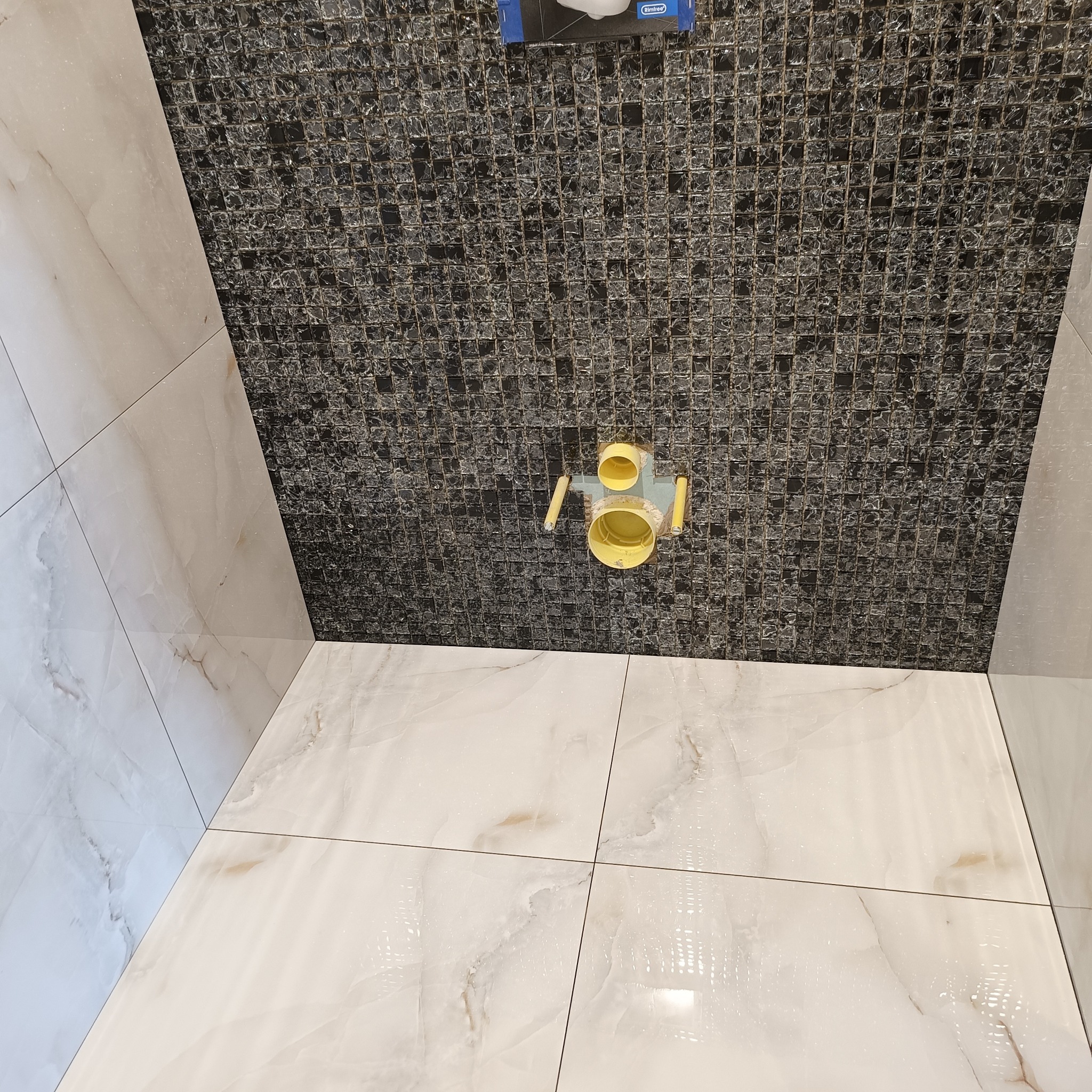 Wykończona łazienka z mozaiką i płytkami imitującymi marmur. Widoczny odpływ liniowy w podłodze. Nietypowe połączenie kolorów i faktur.