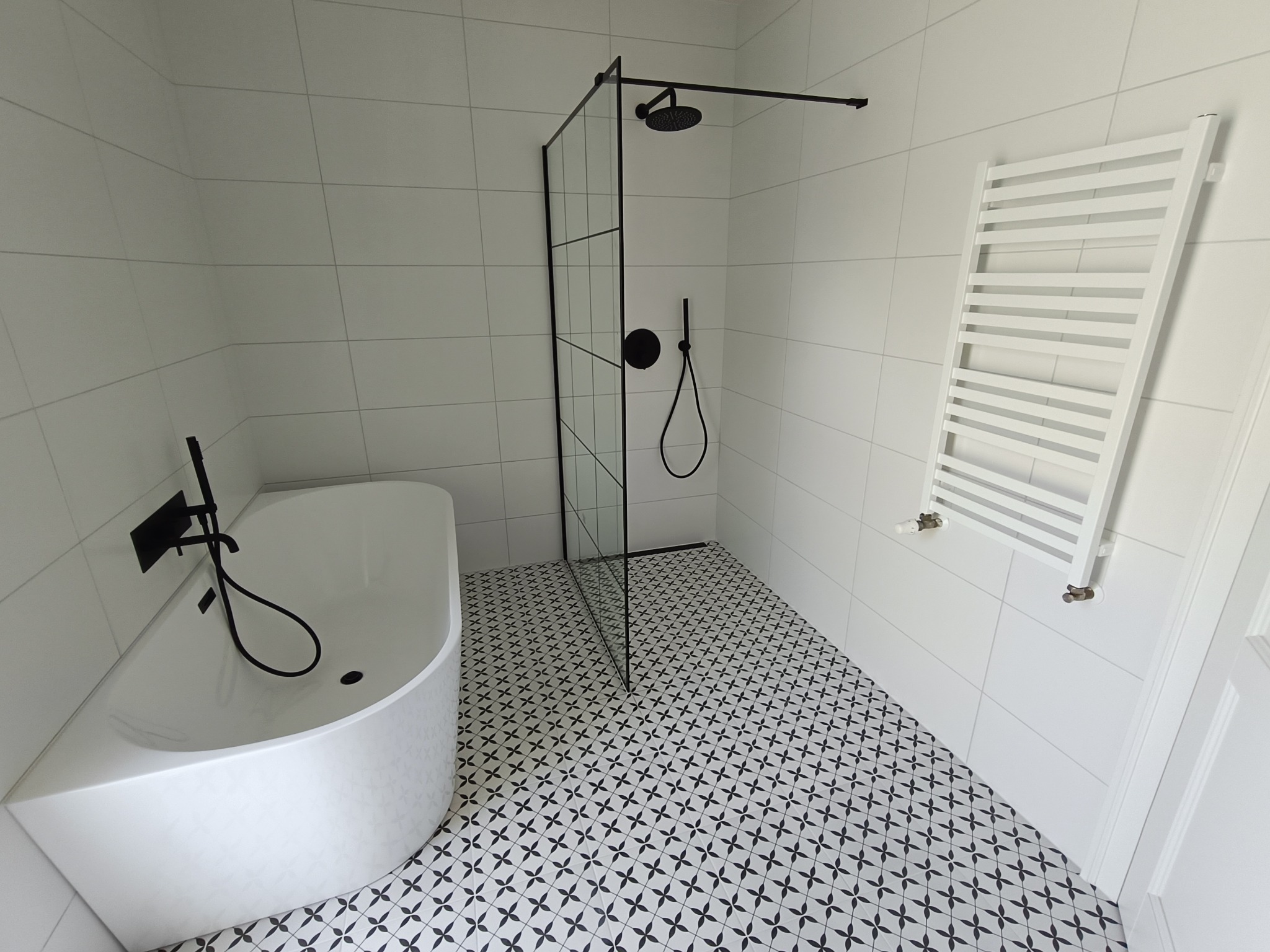 Biała łazienka z czarnymi akcentami: kabina prysznicowa typu walk-in, owalna wanna, wzorzysta podłoga i grzejnik drabinkowy. Minimalistyczny design.