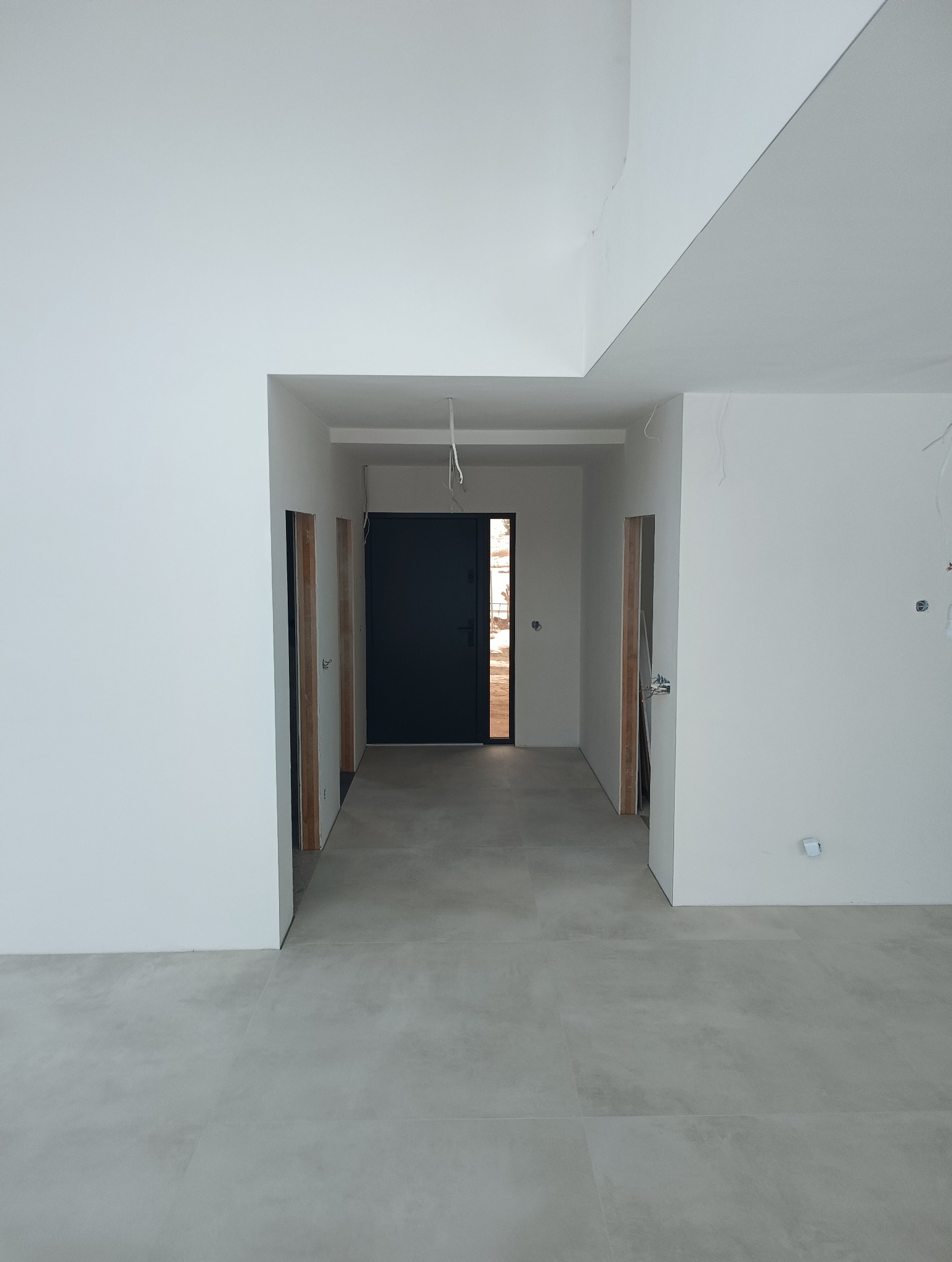 Wykończone płytki podłogowe w korytarzu, widok na drzwi wejściowe. Minimalistyczny design wnętrza w Olesno. Jasne, neutralne barwy.