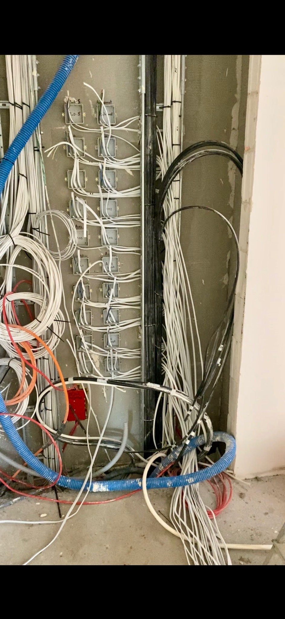 Ściana z zamontowanymi puszkami i przewodami elektrycznymi w trakcie instalacji, widoczne kable w różnych kolorach i peszle. Etap prac instalacyjnych.