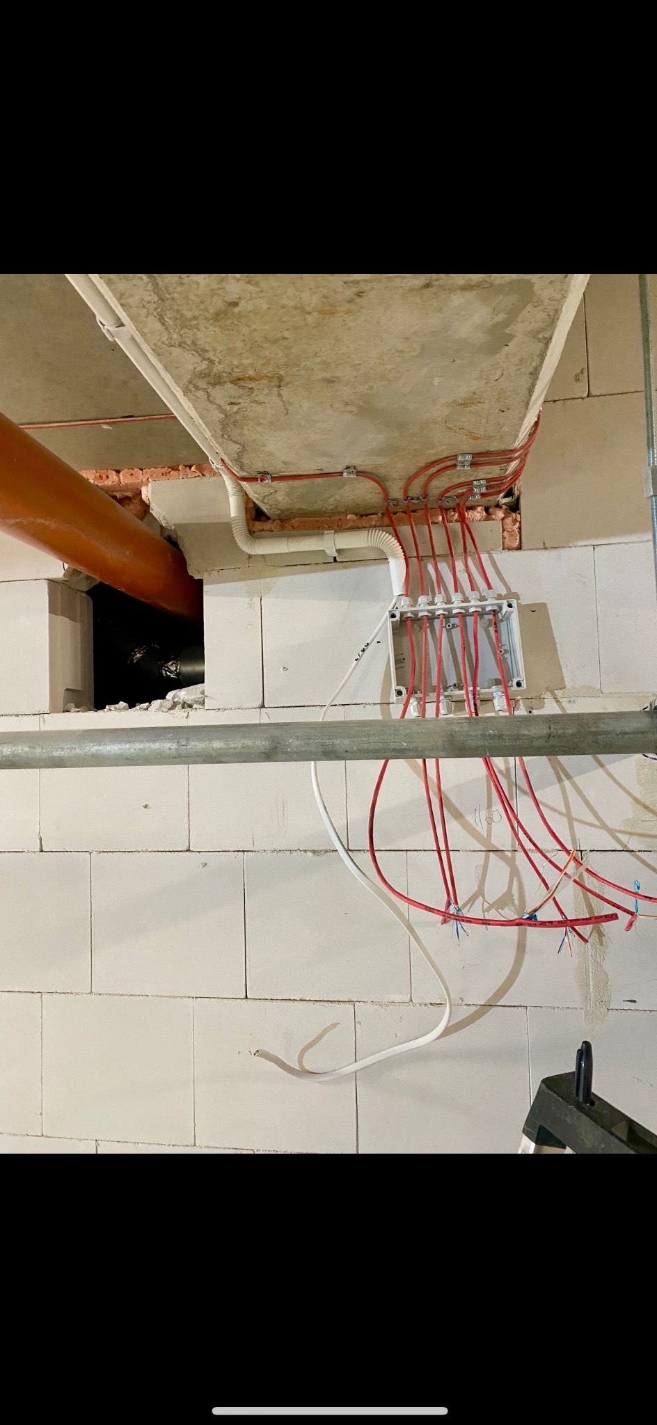 Rozprowadzenie przewodów elektrycznych w puszce pod sufitem, widoczne kable w kolorze czerwonym i białym, zamocowane do ściany z białych bloczków.