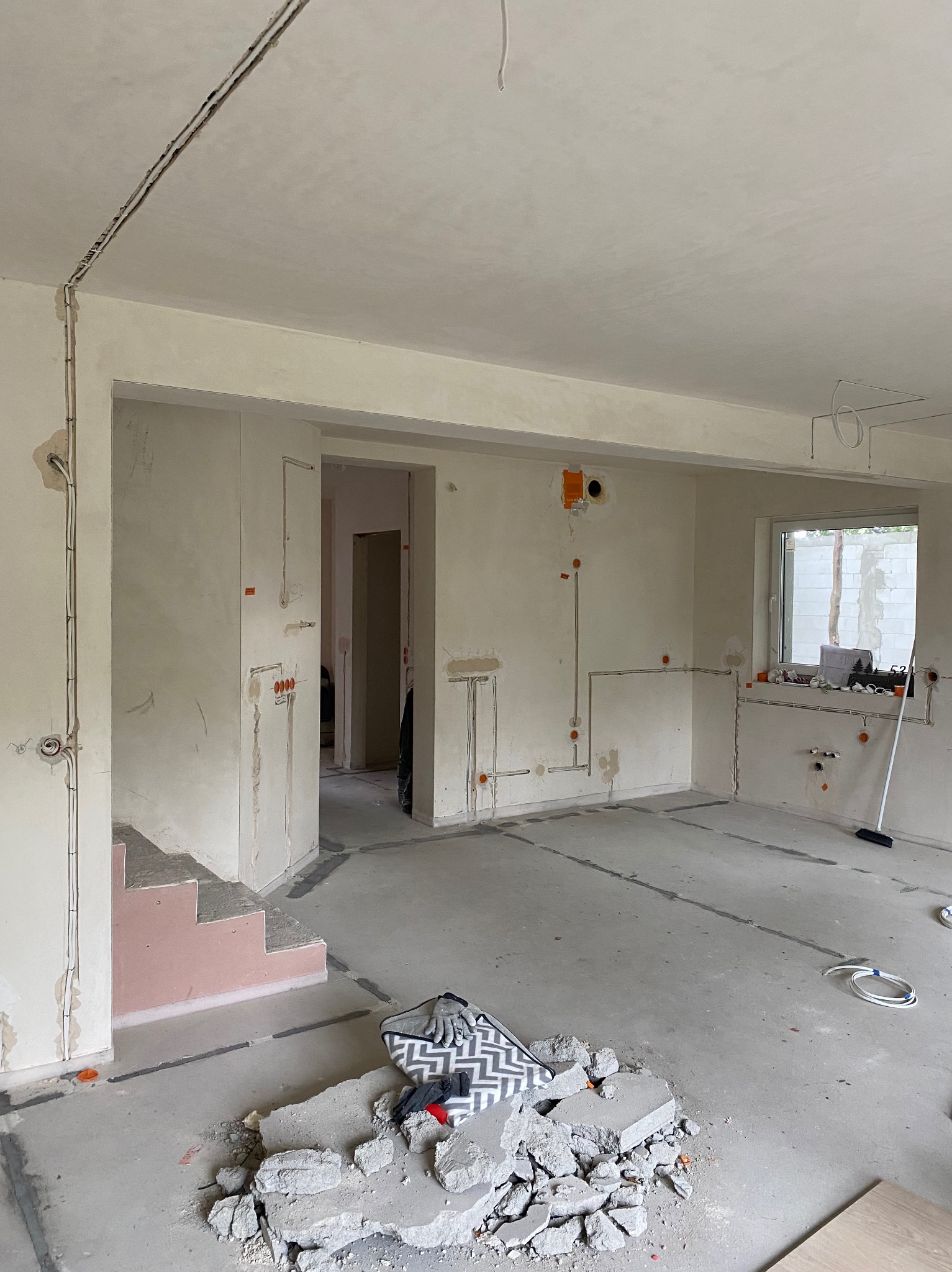 Surowy stan wnętrza z rozprowadzoną instalacją elektryczną po ścianach i podłodze. Widoczne puszki elektryczne, kable w bruzdach i gruz na podłodze.