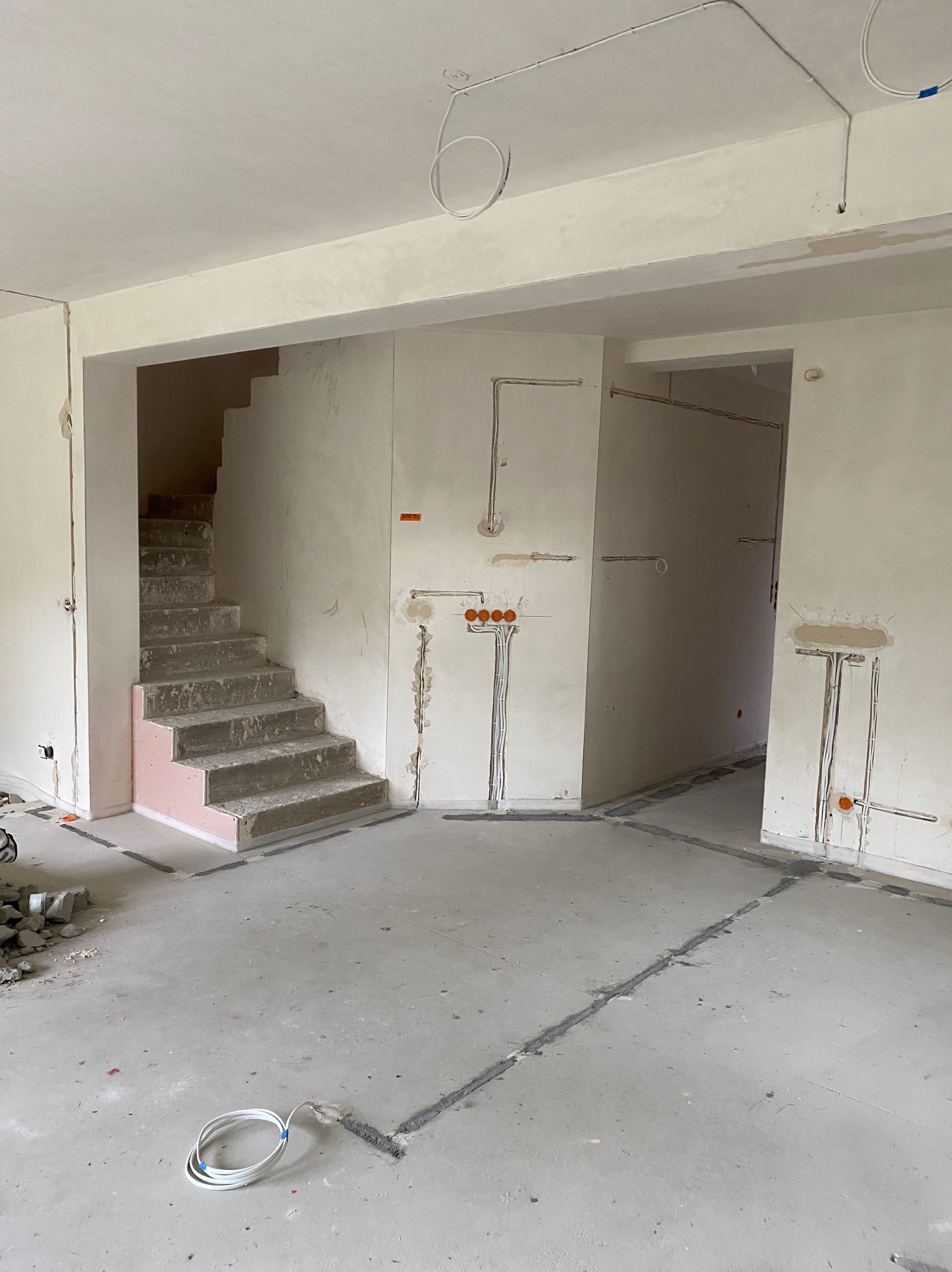 Wnętrze w trakcie prac: widoczne kable elektryczne w ścianach i na suficie, bruzdy w podłodze, surowe schody. Stan surowy, przygotowanie do dalszych prac wykończeniowych.