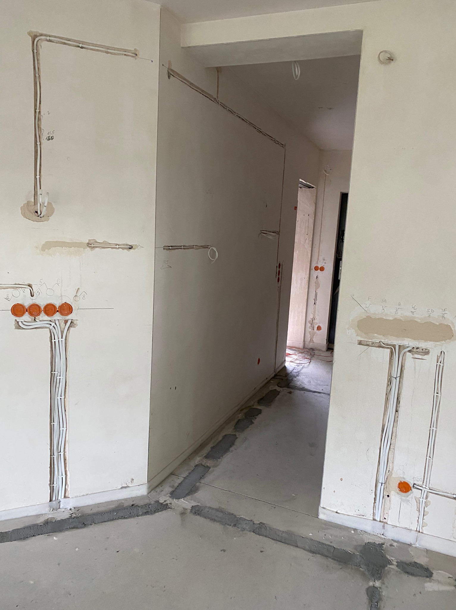 Ściana w trakcie prac elektrycznych: widoczne przewody w bruzdach, pomarańczowe puszki instalacyjne. Surowy stan, przygotowanie do dalszych prac wykończeniowych.
