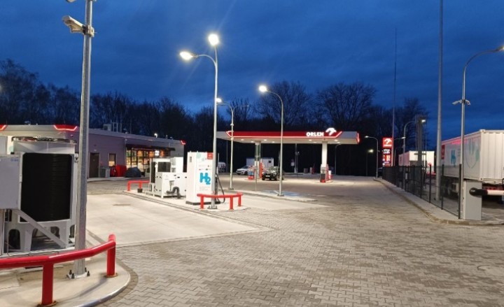 Nowoczesna stacja paliw Orlen z kostki brukowej, oferująca również wodór (H2). Widok na dystrybutory, oświetlenie i budynek stacji o zmierzchu.