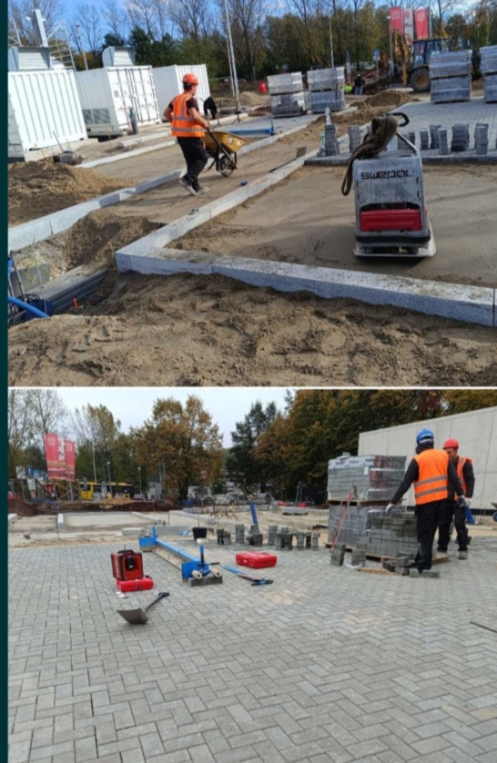 Prace brukarskie w toku: robotnik z taczką, ubijarka, palety kostki. Część terenu wyłożona kostką, widoczne narzędzia i materiały budowlane.