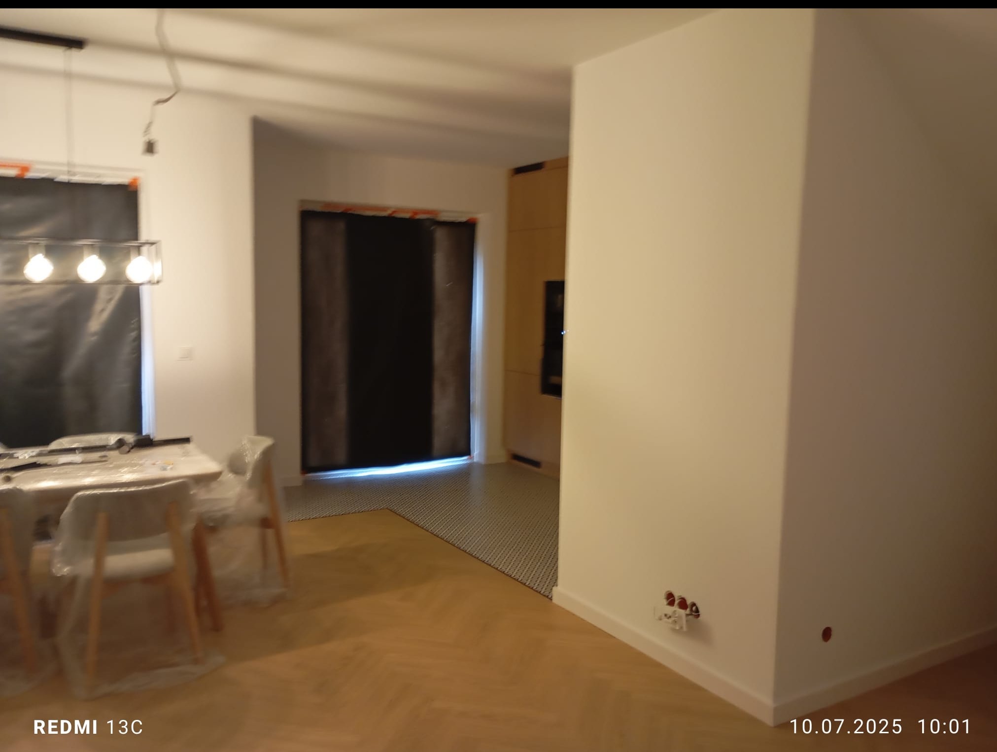 Nowoczesne wnętrze w trakcie wykańczania: parkiet w jodełkę, zabezpieczone meble folią, ściany przygotowane do malowania, widoczne punkty elektryczne.