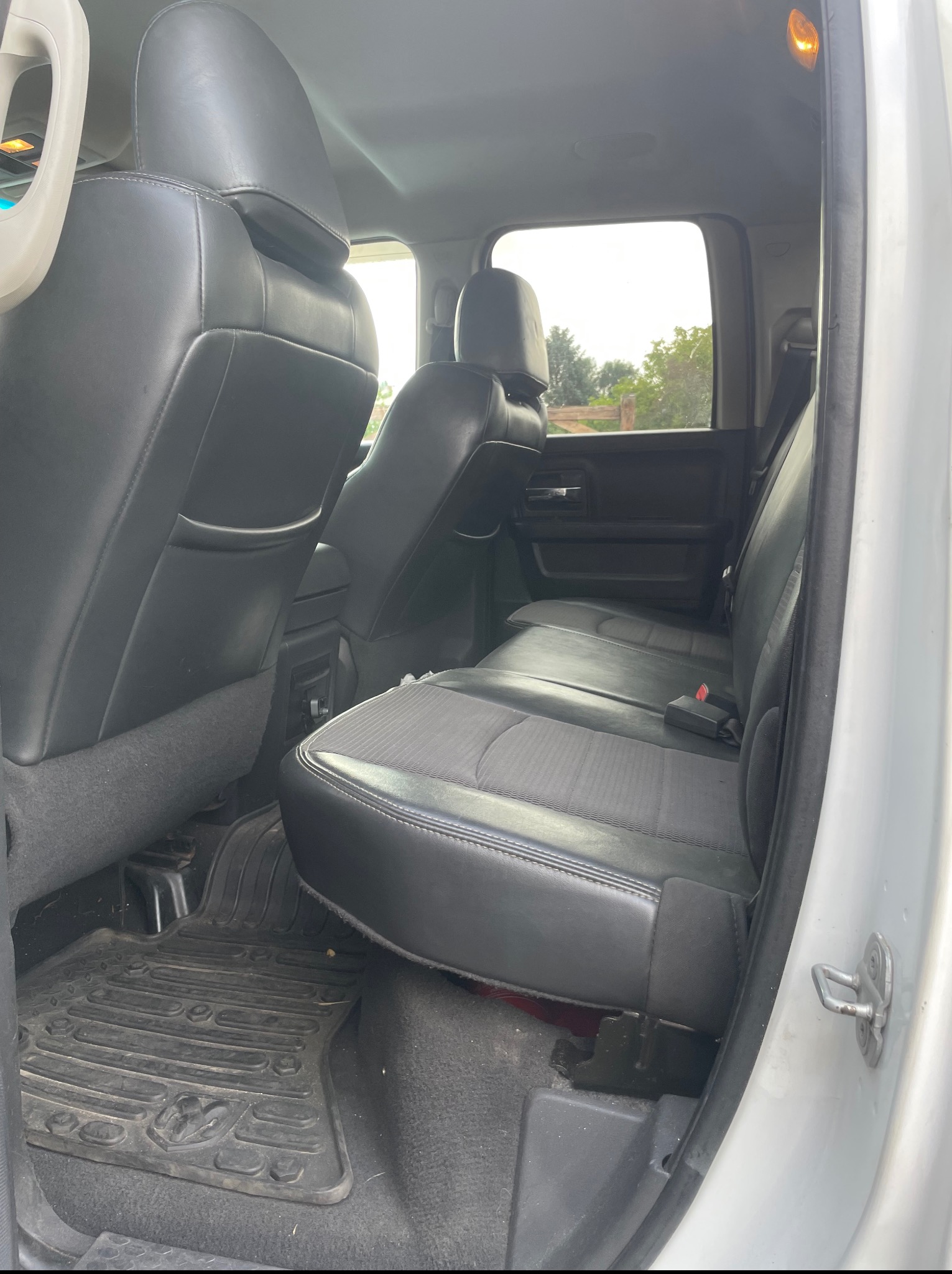 Wnętrze samochodu z czarnymi skórzanymi siedzeniami i gumowymi dywanikami z logo. Widok na tylną kanapę z zapiętym pasem bezpieczeństwa i widokiem na zewnątrz przez okno.