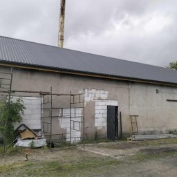 GibDach - Szary dach z blachy trapezowej na budynku gospodarczym, częściowo z drewnianą konstrukcją, widoczne rusztowania i narzędzia, pochmurne niebo w tle.