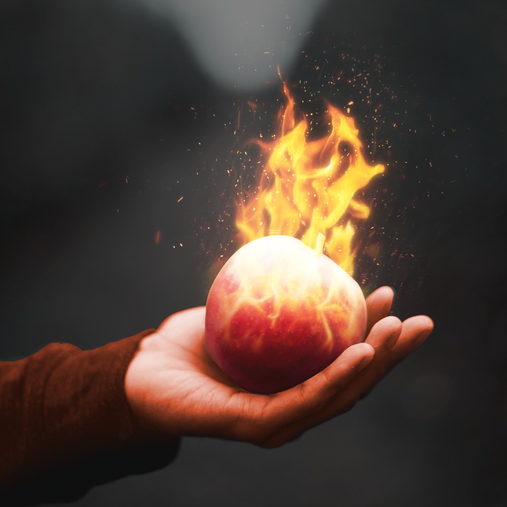 Płonące jabłko w dłoni na ciemnym tle, efekt graficzny. Dynamiczne płomienie, iskry. Praca graficzna.