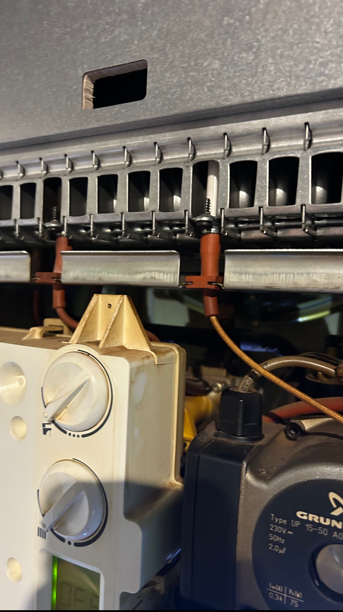 Wnętrze pieca gazowego z widocznymi elementami palnika, dyszami i pompą obiegową, ukazujące skomplikowaną konstrukcję urządzenia.