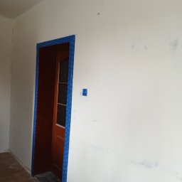 Krzysztof Gardzielik - Przygotowanie do malowania: ściana z resztkami po szpachlowaniu, zabezpieczone drzwi brązowe taśmą malarską, gniazdko elektryczne zaklejone folią.