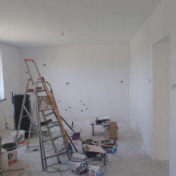 Krzysztof Gardzielik - Świeżo pomalowane na biało wnętrze pokoju z widoczną drabiną, wiaderkami farb i narzędziami malarskimi. Przygotowanie do dalszych prac wykończeniowych.