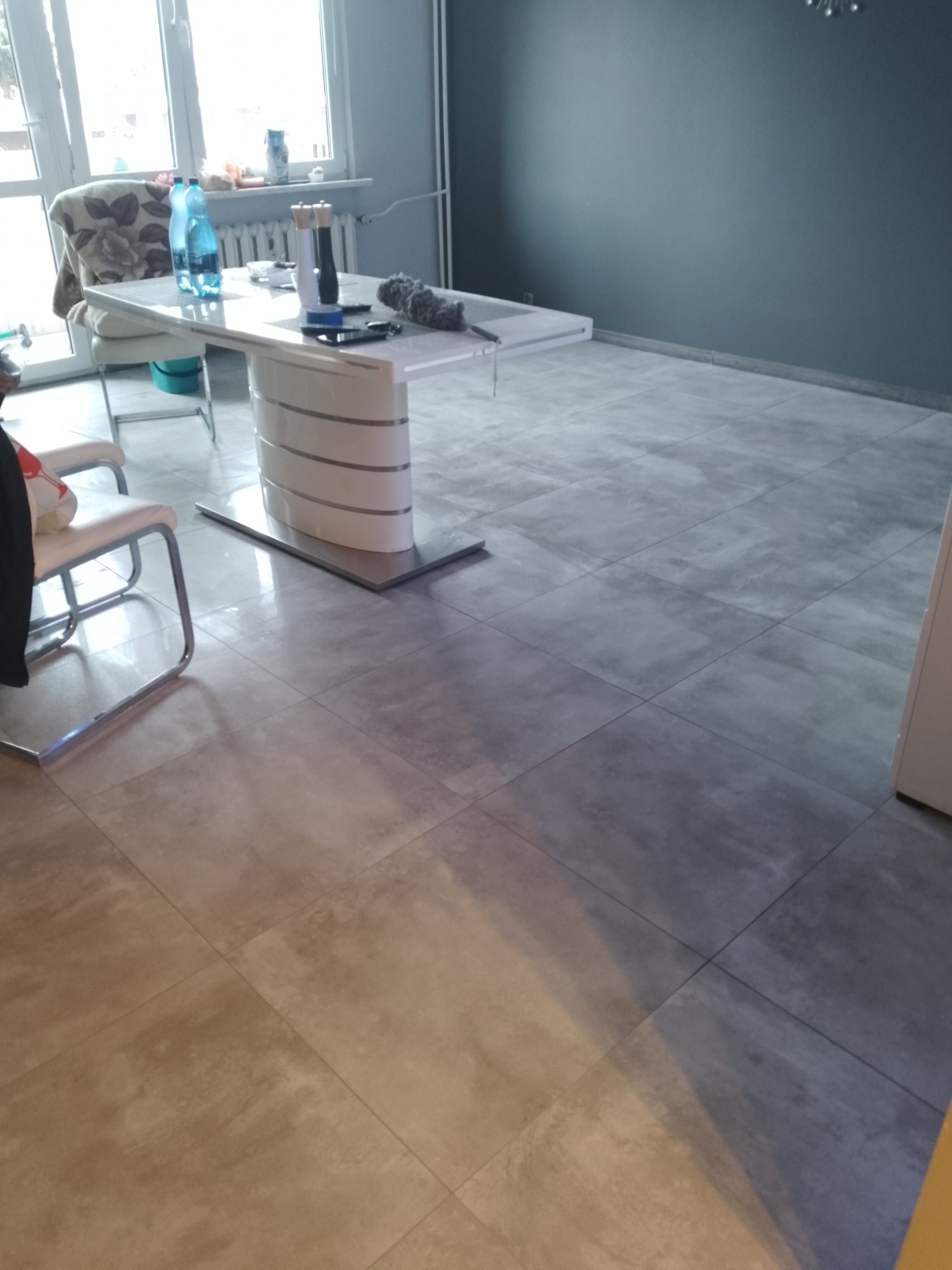 Jasne, wykończone płytkami podłogowymi wnętrze w Siewierzu. Widoczny stół z krzesłami, ściana pomalowana na szaro. Minimalistyczny design.