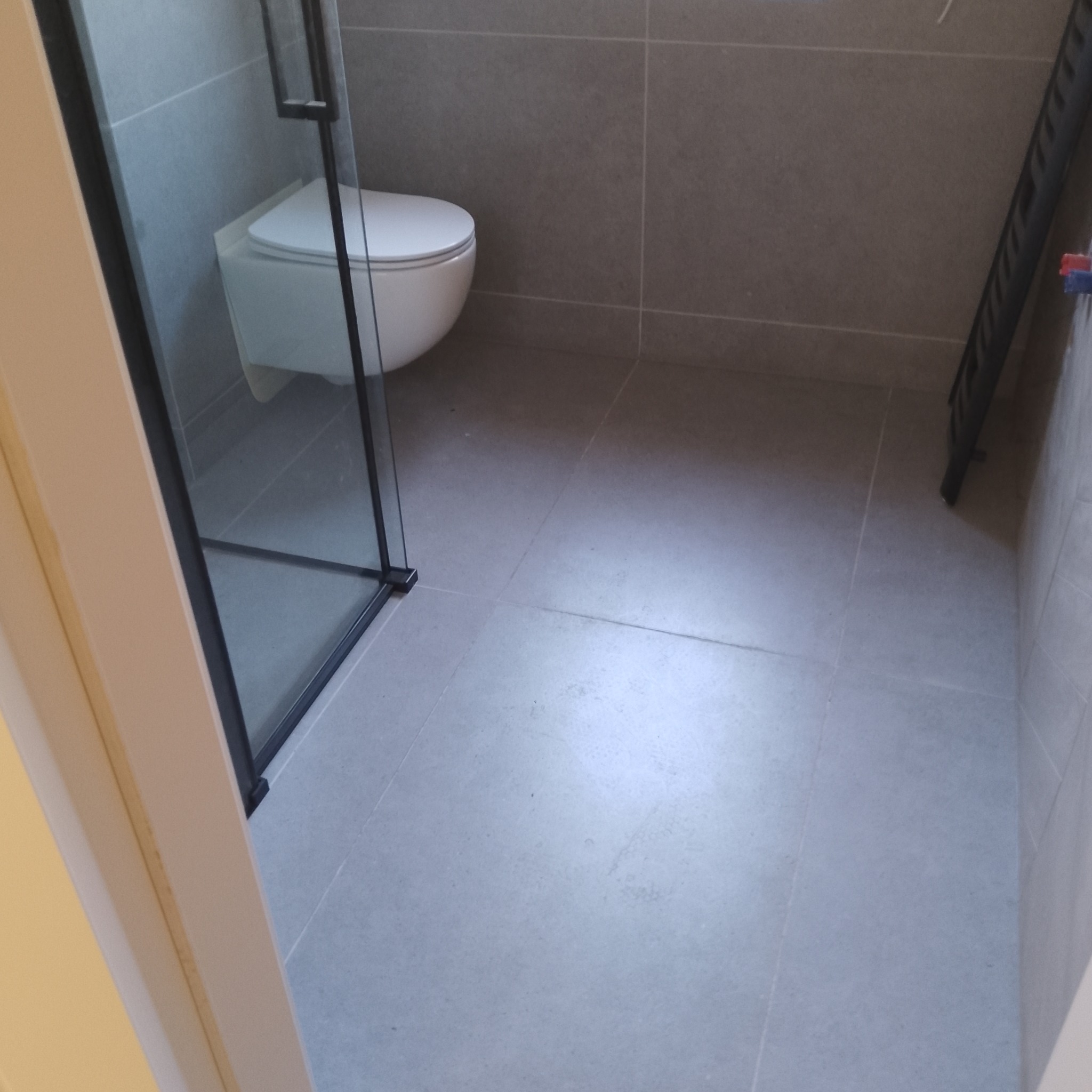 Nowoczesna łazienka z szarymi płytkami, podwieszaną toaletą i kabiną prysznicową z czarnymi ramami, ukazująca minimalistyczny design i dbałość o detale.