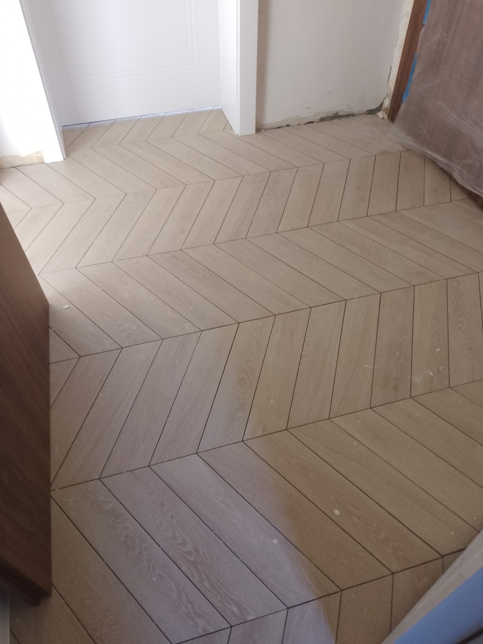 Ułożona podłoga z paneli w jodełkę francuską, jasne drewno. Widoczne fragmenty ścian i drzwi.