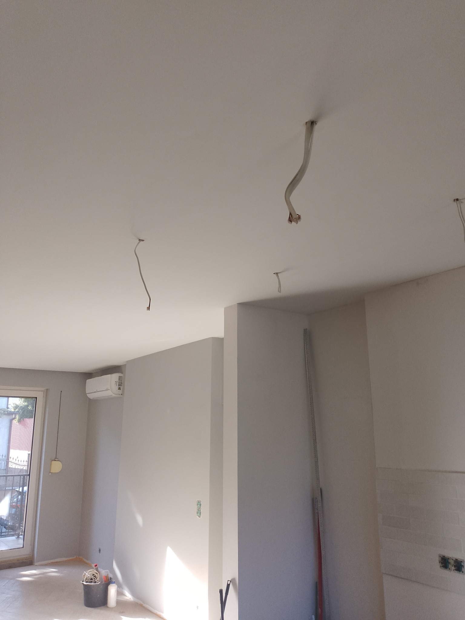 Wnętrze w trakcie prac wykończeniowych: świeżo pomalowane ściany w odcieniach bieli, widoczne przewody wystające z sufitu, przygotowane do montażu oświetlenia.