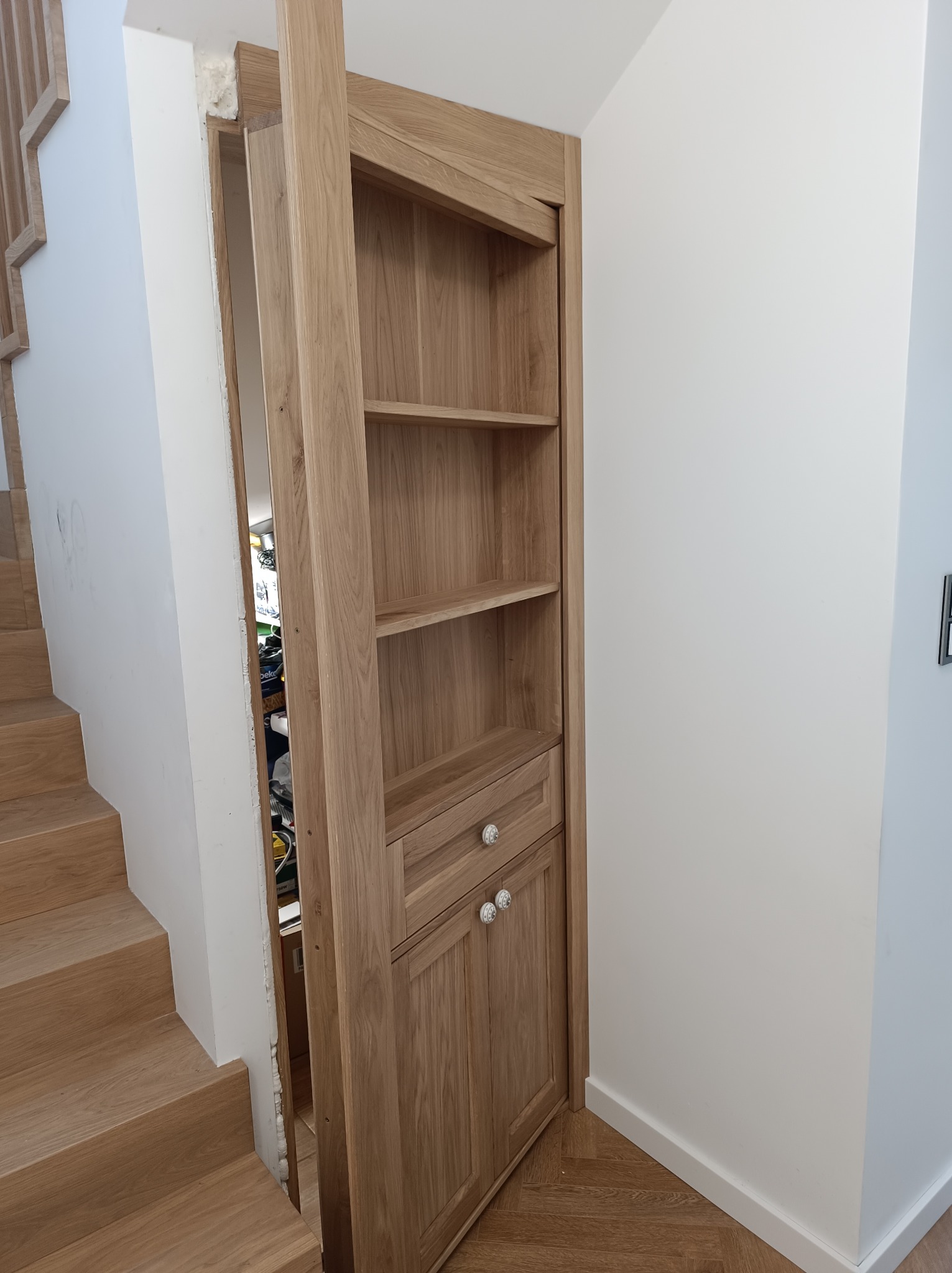 Ukryte drzwi drewniane z półkami, zintegrowane ze schodami w Starachowicach. Nietypowe rozwiązanie stolarskie, oszczędność przestrzeni, naturalne drewno.